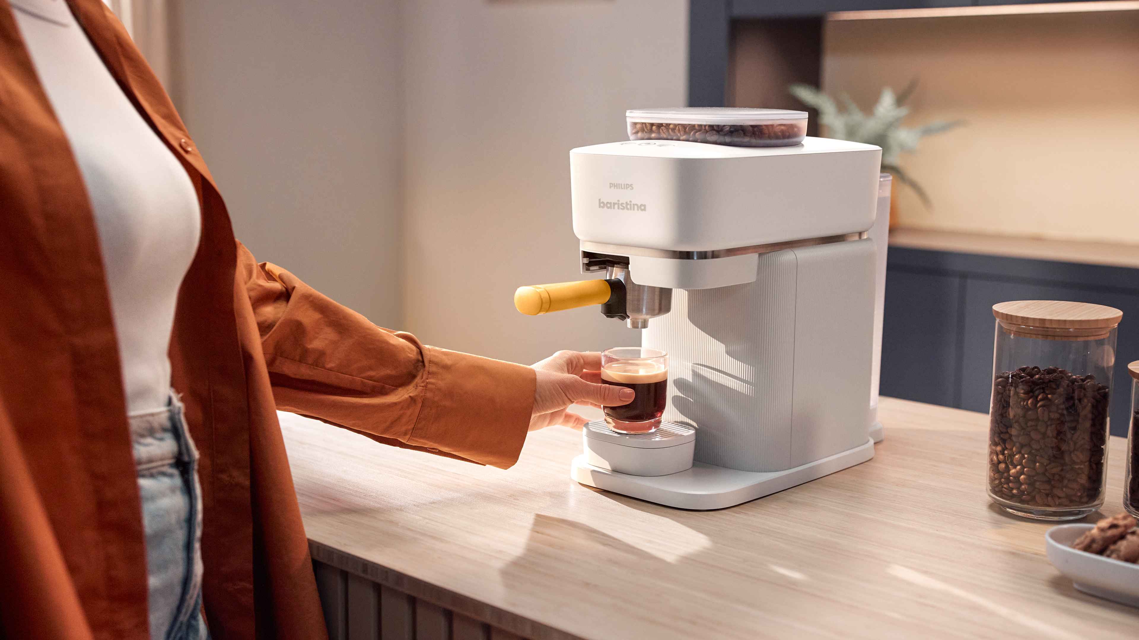 Philips Baristina Espressomaschine brüht reichen Kaffee in eine Glas Tasse, gehalten von einer Person. Philips Baristina Espressomaschine brüht reichen Kaffee in eine Glas Tasse, gehalten von einer Person.